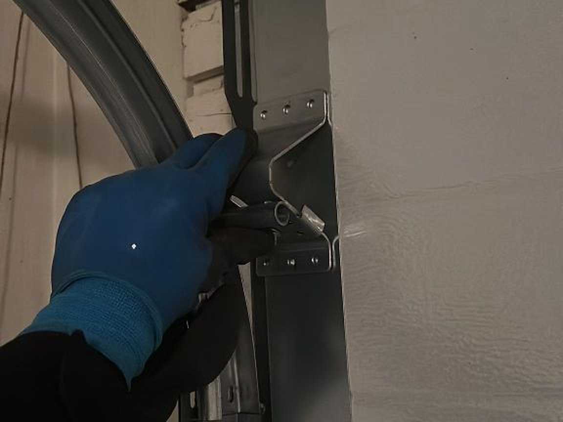 Gloved hand steadying the curved track at the flag bracket during a garage door maintenance visit