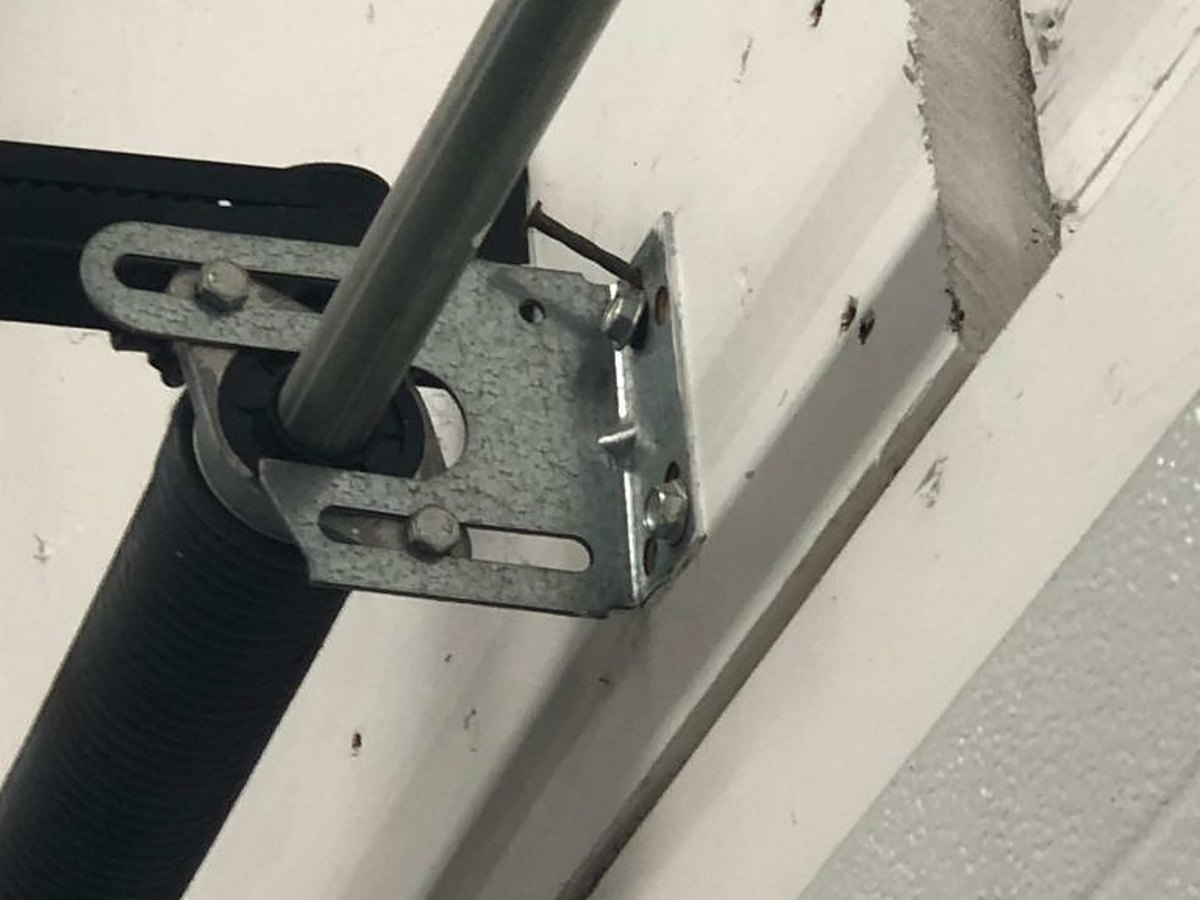 Centre bearing bracket and torsion spring end on a residential garage door, the shaft seated in its bearing and the bracket fixed back to the header