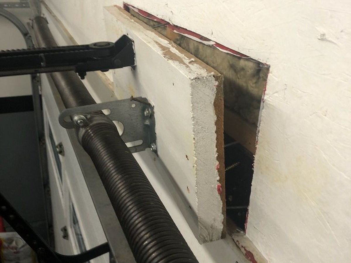 Garage door spring repair under way with the header wall opened up to reach the structural backing behind the spring anchor bracket