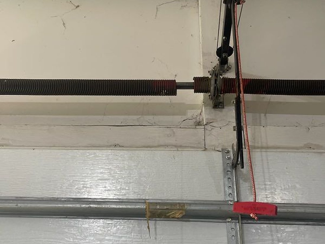 Torsion springs on the shaft above a residential garage door, with the centre bearing plate, both cable drums and the red emergency release cord in view